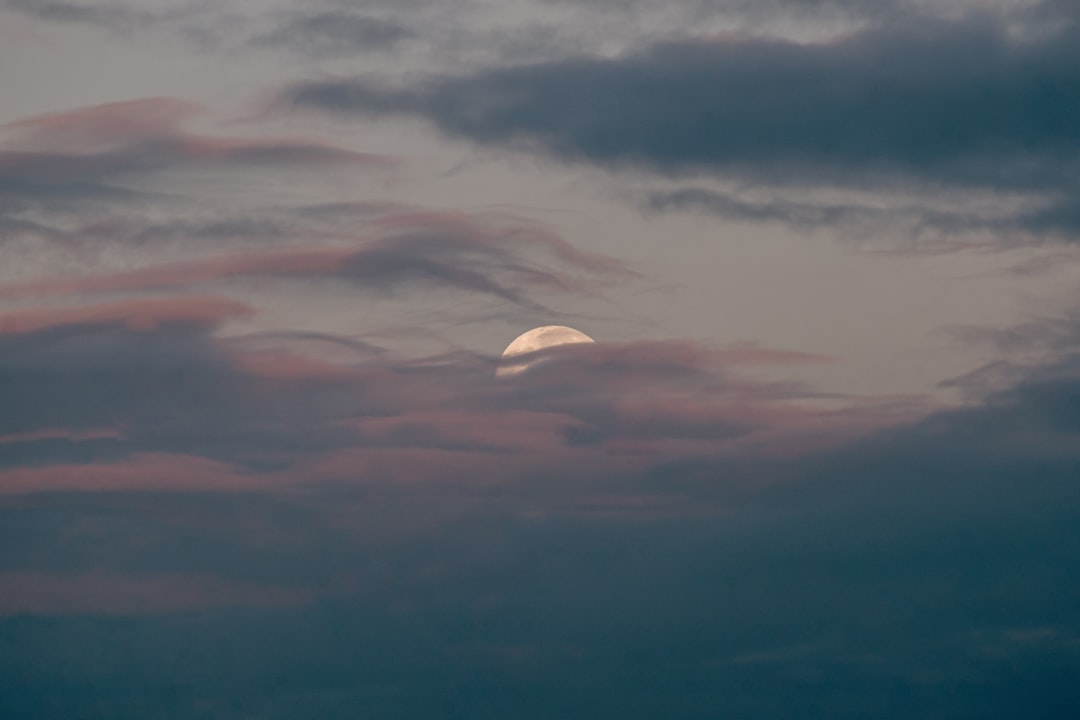 Photo by Sebastian Laverde a full moon is seen through a cloudy sky